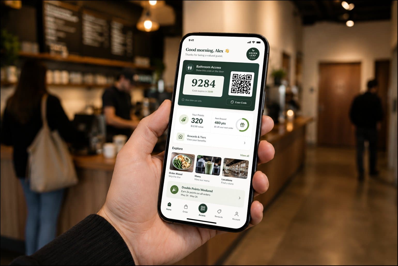 A customer holds their phone displaying a coffee shop loyalty app with a bathroom access code.